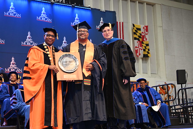 Kofi Simmons receiving the Creative Achievement award from President Wilson and Provost Yu at Fall 2025 graduation