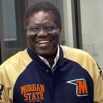 a smiling Dr. Edet Isuk, newly retired Director of Research Compliance and former Chief of Staff to the VP for D-RED, proudly wearing a new Morgan State University jacket