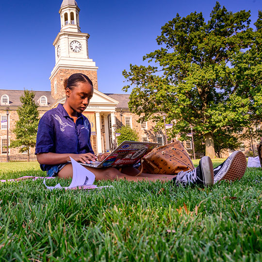 female student sitting in the grass on laptop